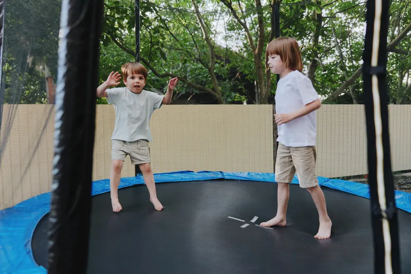 Two cheerful kids jumping on a trampoline, enjoying a sunny day in a vibrant outdoor setting. Their bright clothing adds to the fun atmosphere.