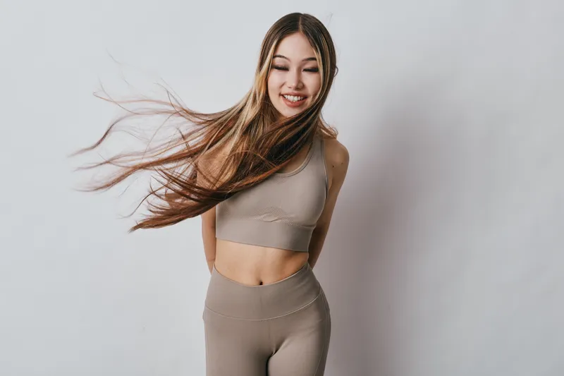 Young woman with long hair smiling and posing in sport outfit on neutral background. Fitness, happiness and youth with motion and casual activewear for lifestyle and health.