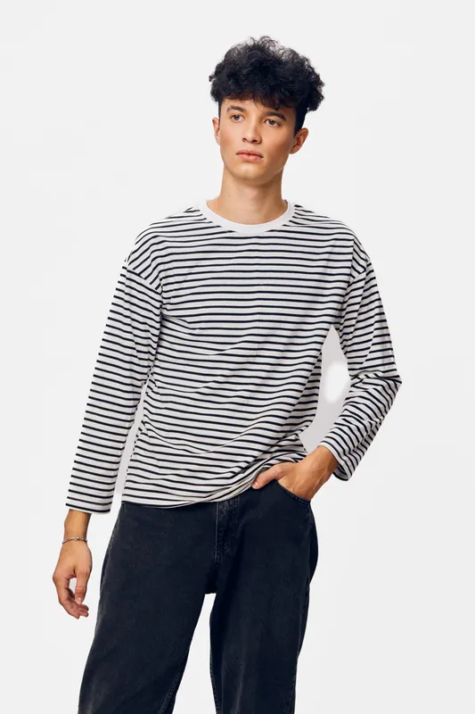 young man wearing striped long sleeve shirt standing with hand in pocket against white background, casual style with curly hair and relaxed posture