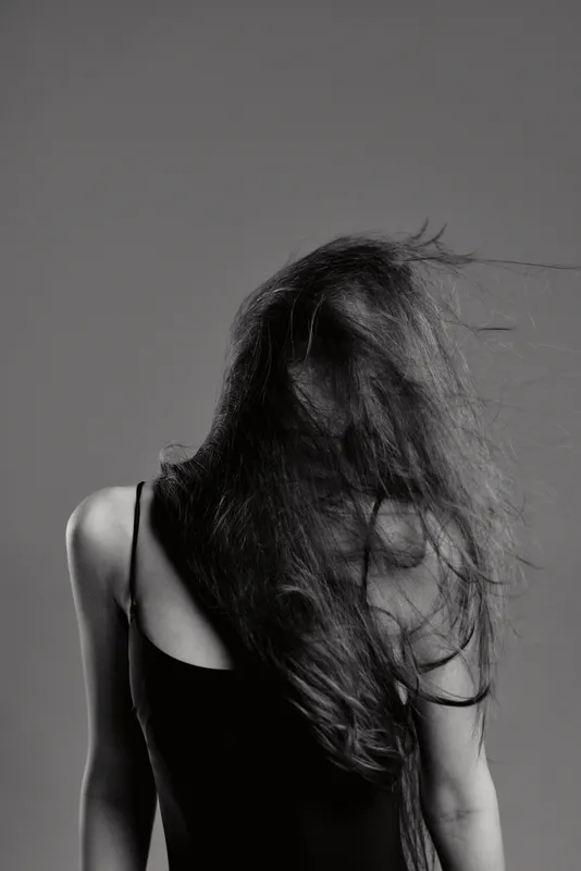Black and white portrait of a woman with flowing hair wearing a sleeveless top, expressing motion and emotion in a minimalistic style.