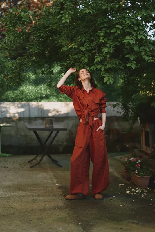 Cheerful woman outdoors in a red jumpsuit, relaxed pose under sunlit greenery, soft breeze, natural colors, candid lifestyle moment