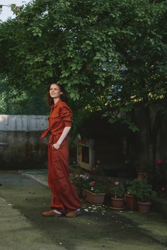 Smiling woman in a red dress stands outdoors in a lush garden, capturing a chic lifestyle moment with confidence, elegance, and relaxed charm