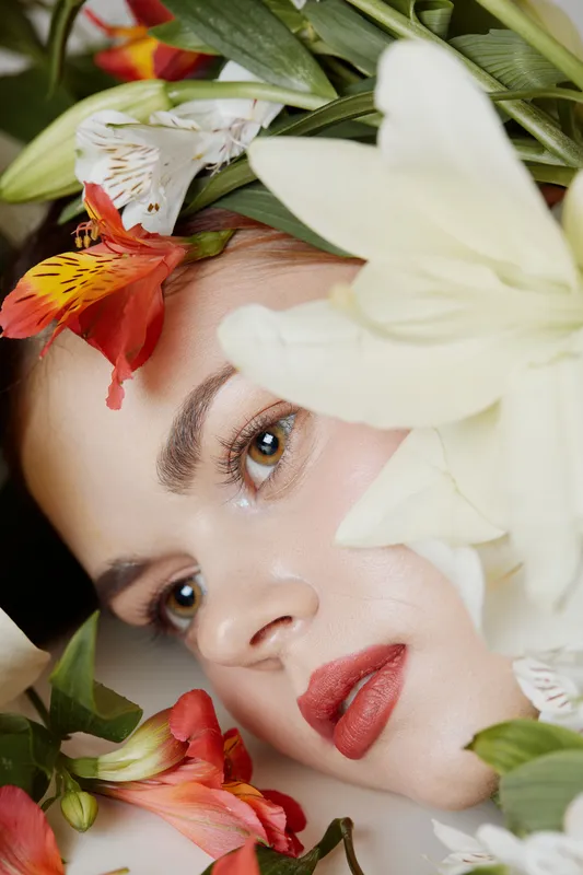 Beautiful girl with natural makeup surrounded by vibrant flowers, capturing a serene and refreshing spring atmosphere with soft colors and gentle emotions