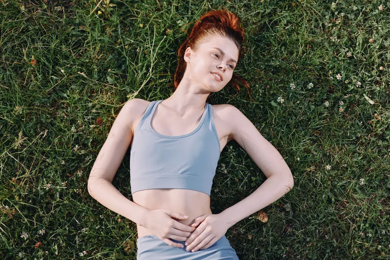 Young athletic woman in blue sportswear lying on green grass, radiating relaxation and peace in a vibrant outdoor setting during summer
