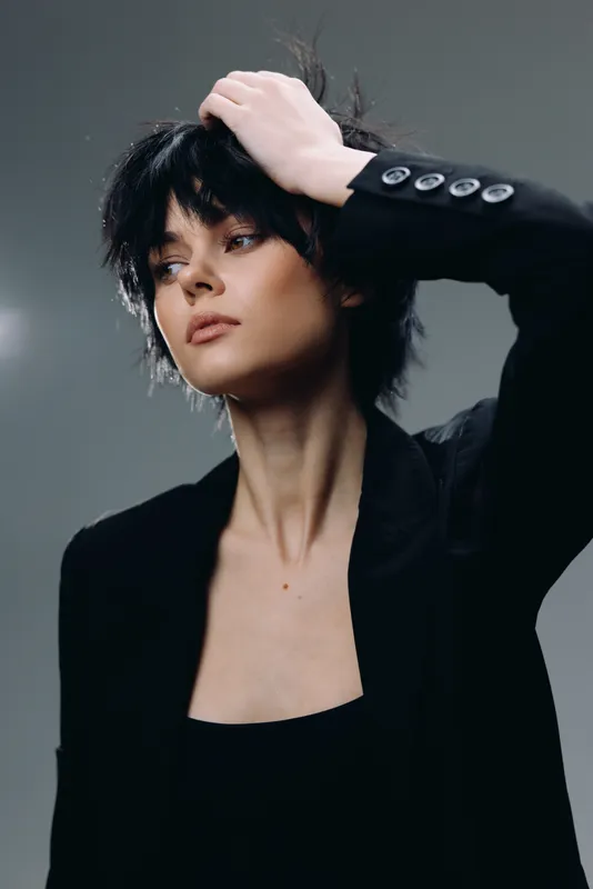 Stylish woman with short dark hair posing in black blazer with thoughtful expression and moody lighting.