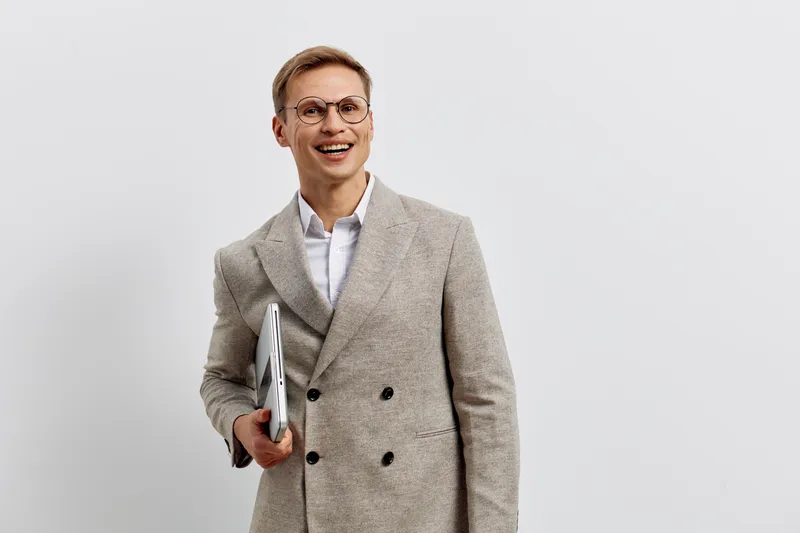 Smiling man holding laptop wearing beige coat glasses look aside casual style studio portrait digital nomad technology concept