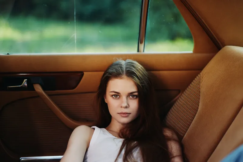 Young woman with long hair relaxing in a classic car, conveying tranquility and nostalgia against a lush green background, perfect for lifestyle themes.