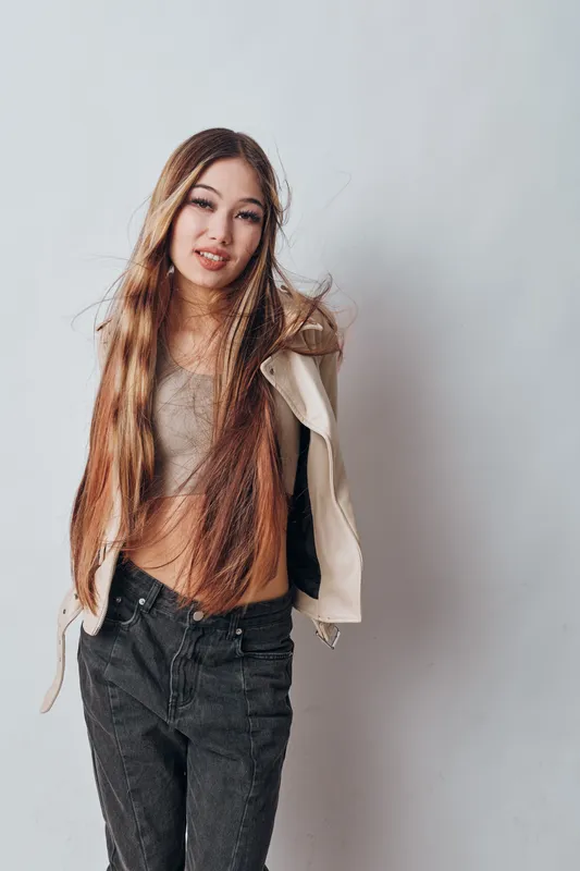 Young woman standing with long hair and casual clothes looking at camera against light wall background. Portrait of female model with natural makeup and relaxed pose indoors.