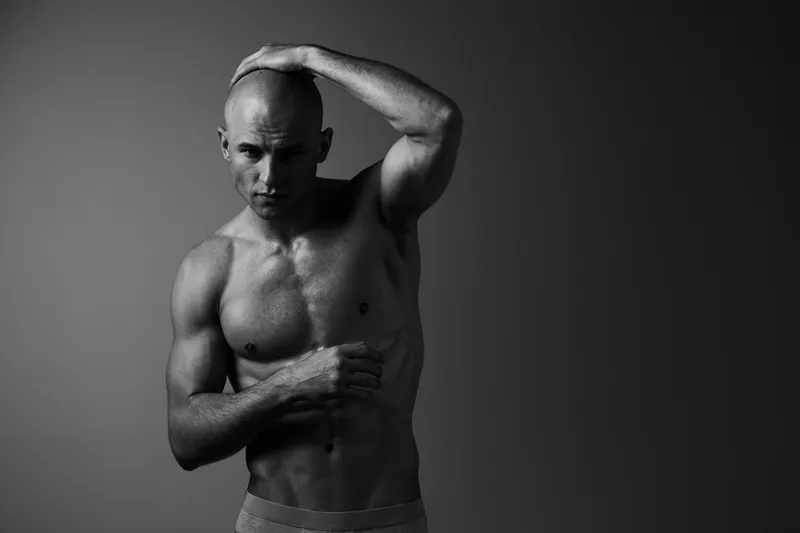 Artistic black and white portrait of a muscular man posing confidently, emphasizing strength and emotion through dramatic lighting and shadows.