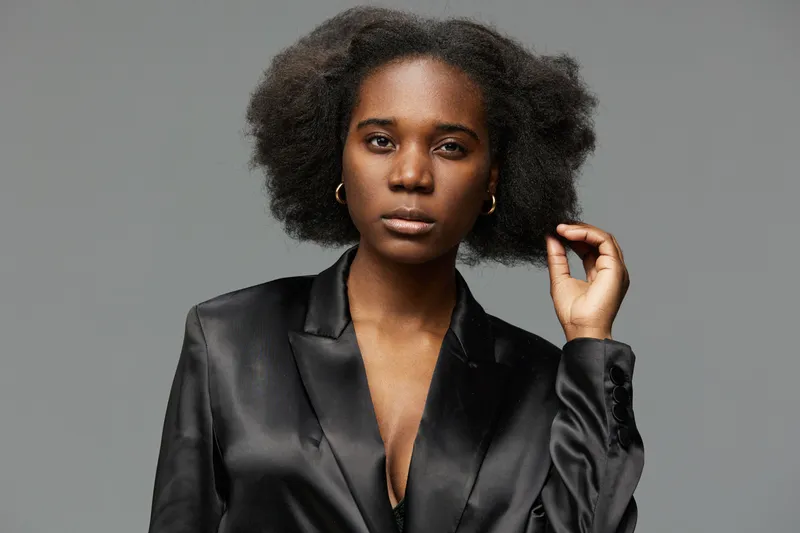 Elegant black model in a stylish satin jacket, showcasing natural hair with confidence against a soft grey background