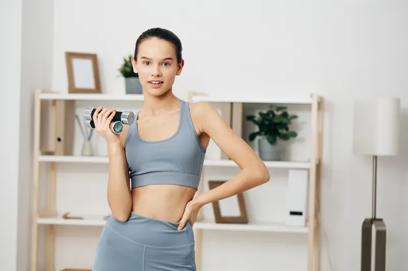 Woman fitness sport workout training health motivation: a confident athlete lifts a dumbbell in a clean home gym, wearing athletic wear. Focused posture amid minimal decor showcases training and
