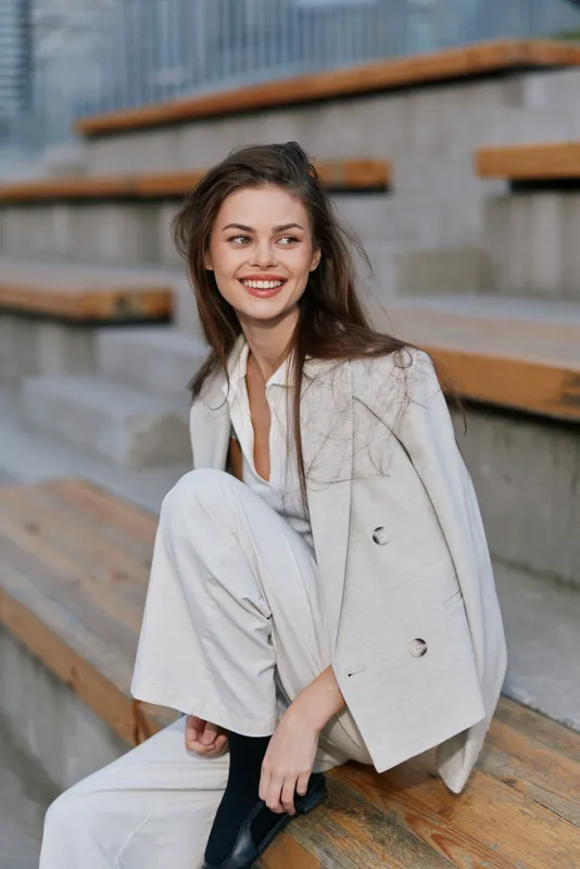smiling woman in beige business casual outfit sitting on urban wooden steps with confident expression fashion style outdoor autumn
