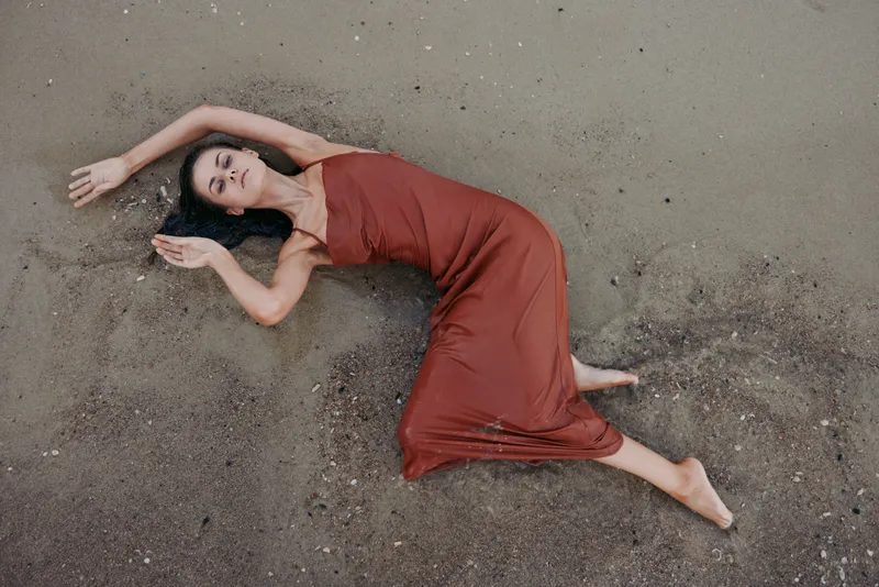 Relaxed woman in a red dress lying on sandy beach, showing calmness, serenity, and natural beauty in warm tones.