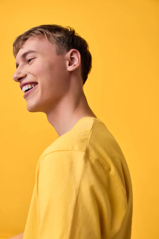 Smiling man in a yellow shirt stands against a bright yellow backdrop, exuding casual style, cheerful mood, and sunny vibe perfect for lifestyle, fashion, and positive branding imagery