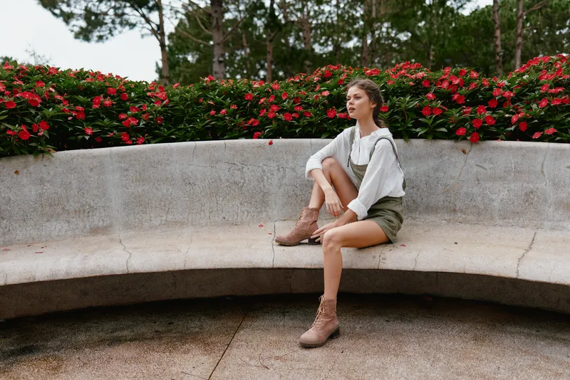 Young woman sitting on a bench surrounded by vibrant flowers, showcasing a relaxed vibe with autumn fashion