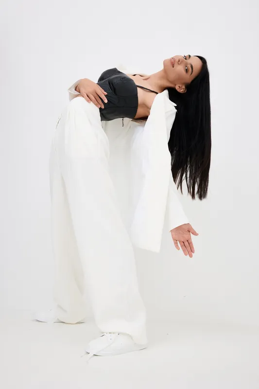 woman posing in stylish white suit with black top, long dark hair, contemporary fashion, studio background, dynamic posture expression