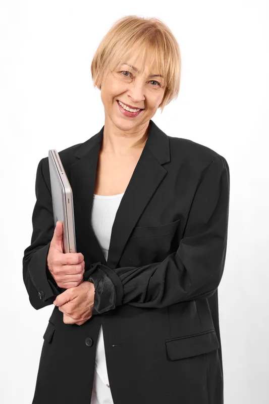 Mature woman smiling while holding book, wearing black blazer and white top, studio portrait on white background, calm education concept, looking at camera confidently