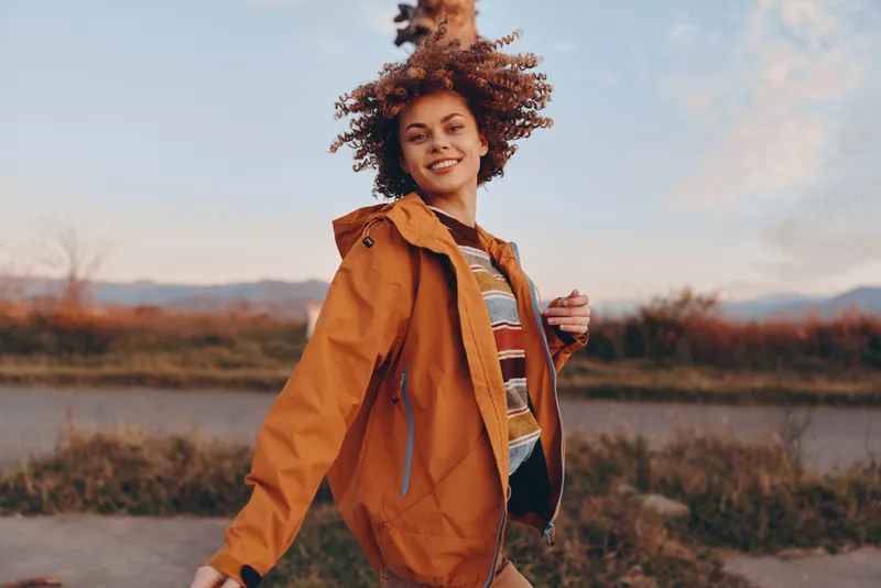 Woman lifestyle outdoors hiking walking, backpack jacket autumn nature, young female smiles while hiking on countryside trail, rucksack and warm coat, scenic river and open sky