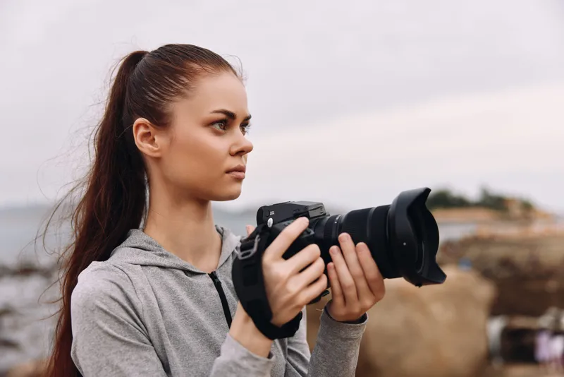 Young woman in sportswear holding a camera by the seaside, demonstrating focus and determination Ideal for travel and lifestyle photography