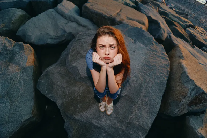 lifestyle woman in modern boho-western denim street style sitting on large rocks, film color effect enhancing natural textures and relaxed mood