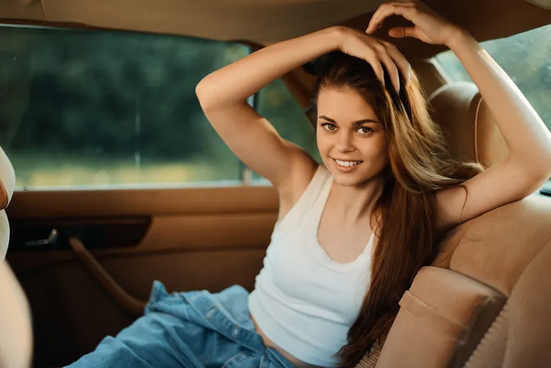 Young woman with long hair wearing casual outfit, smiling in a car, showcasing confidence and relaxation in a natural setting.