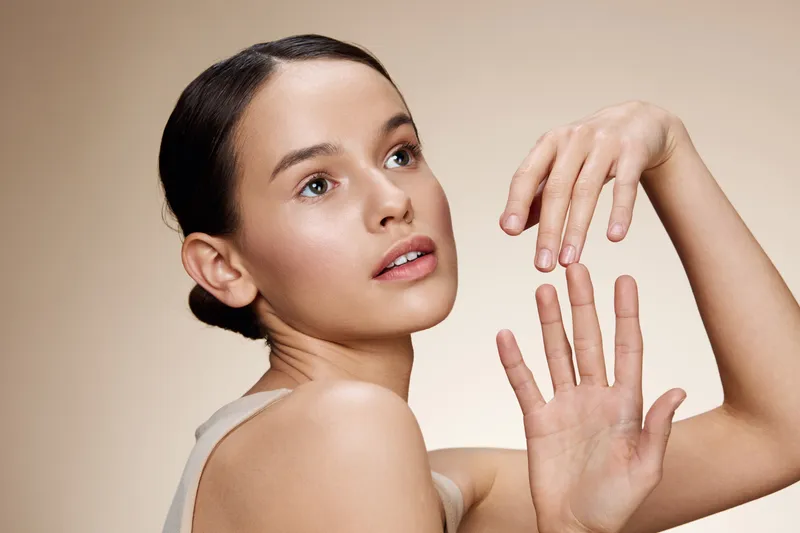 Elegant young model showcasing natural beauty with soft makeup and neutral toned background, expressing serenity and confidence