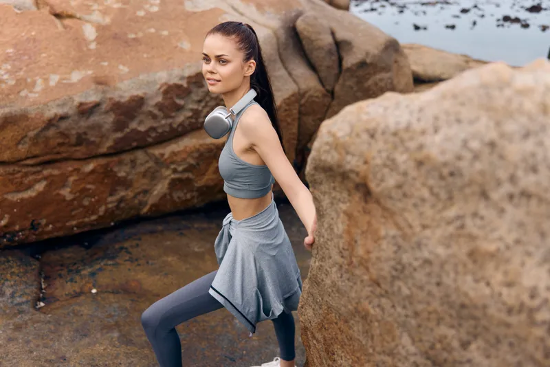 Active young woman in sportswear climbing rocks by the sea, showcasing determination and strength, with a focus on fitness and health concepts