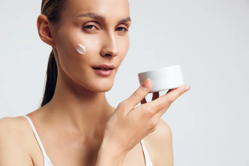 Woman skincare cream face beauty cosmetic wellness spa routine care in a bright studio close up with white moisturizer on cheek and soft studio light concept for hydration