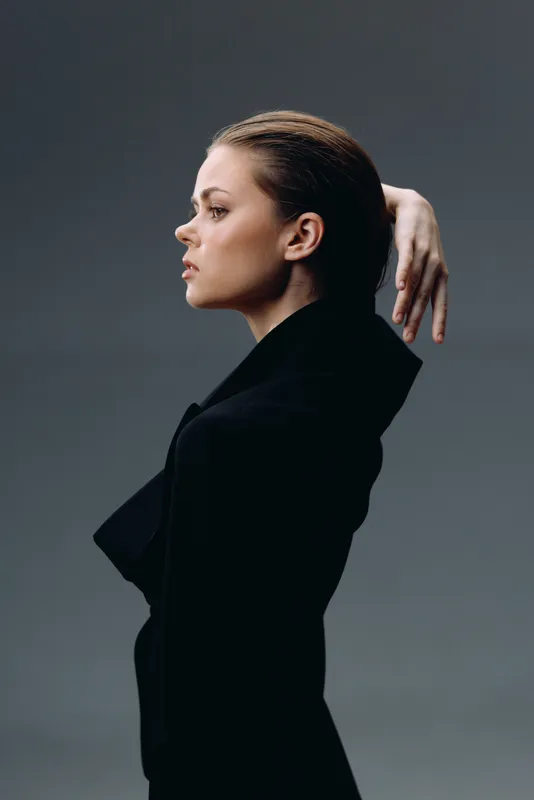 Profile of a thoughtful woman in black clothing with sleek hairstyle and neutral expression on gray background