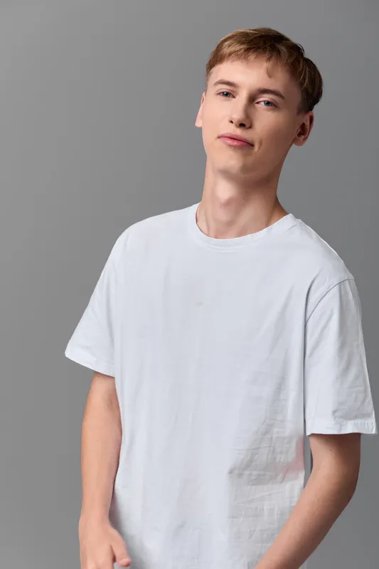 Young man in a white t shirt stands in a neutral studio with soft lighting, casual style, relaxed pose, ready for lifestyle use and everyday fashion visuals