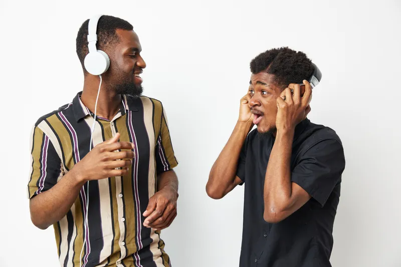 Two smiling African American men enjoying music together, showcasing joy and friendship in a vibrant setting, perfect for promoting togetherness and fun moments.