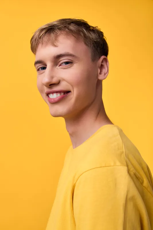 Smiling young man in a yellow sweater against a yellow backdrop, conveying casual fashion, friendly expression, and confident energy for lifestyle branding
