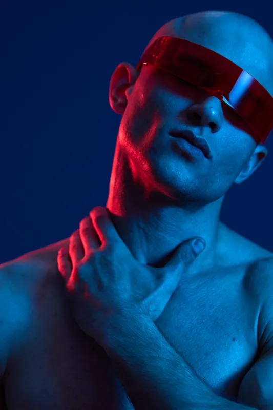 A striking portrait of a man wearing futuristic sunglasses, showcasing a unique blend of blue and red lighting, creating a dramatic and captivating atmosphere.