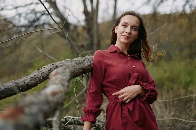 An authentic portrait of a calm, confident woman leaning on a rustic fence, captured in a woodland setting to convey genuine charm, natural style, and believable mood.