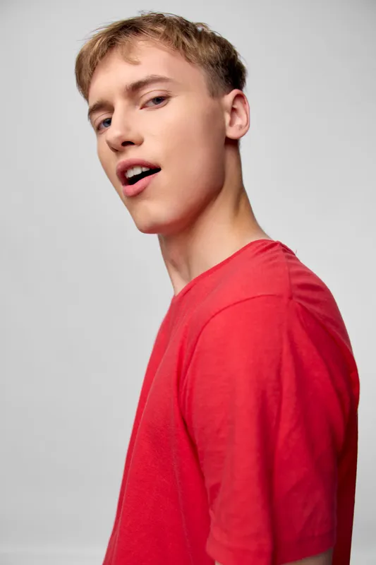 Young man in a red shirt strikes a casual pose with a confident expression in a clean studio setting, ready for lifestyle or fashion use, with crisp lighting and a neutral background