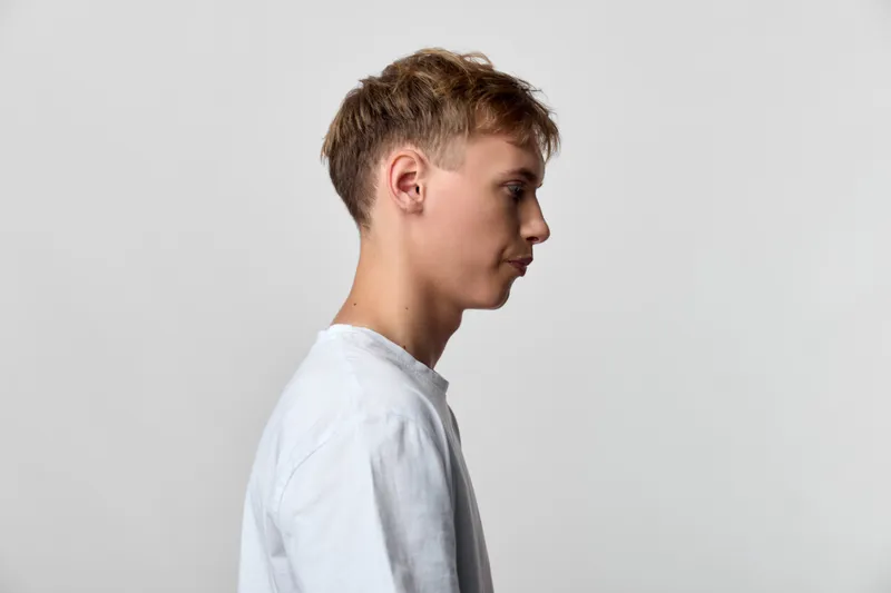 Profile view of a young man in a white shirt against a plain backdrop, conveying calm, focus and minimalism, suitable for lifestyle, fashion, and creative concepts in stock photography