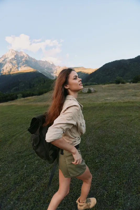 Young woman traveler with backpack hiking in mountains enjoys nature and fresh air during outdoor adventure in summer, lifestyle concept with positive mood and freedom feeling
