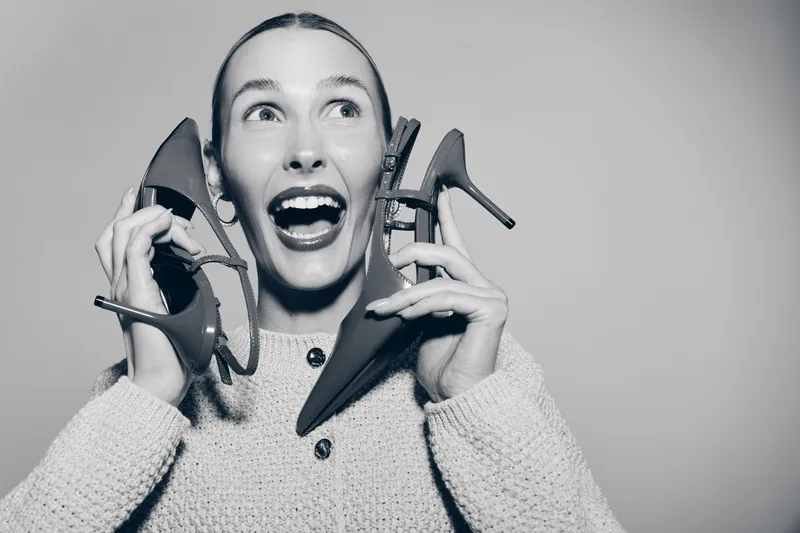 Happy Caucasian woman with light skin holding two high heel shoes near her face. Concept for fashion, style, shopping, and excitement.