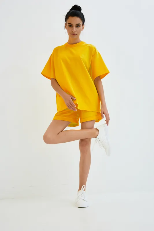 young woman in bright yellow casual outfit stretching leg in minimalist white space, athletic pose, comfortable style, fitness, active lifestyle, indoors