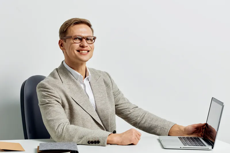 smiling man working digital nomad laptop glasses business casual look at camera sitting chair white background remote work concept
