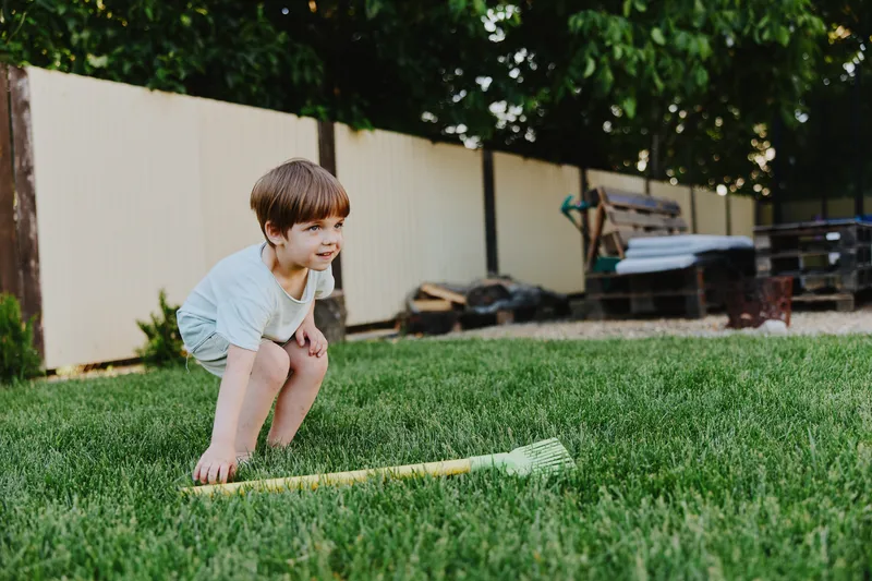 Happy boy playing in the garden with a rake, enjoying nature and outdoor activities on a sunny day, surrounded by vibrant greenery and a playful atmosphere.