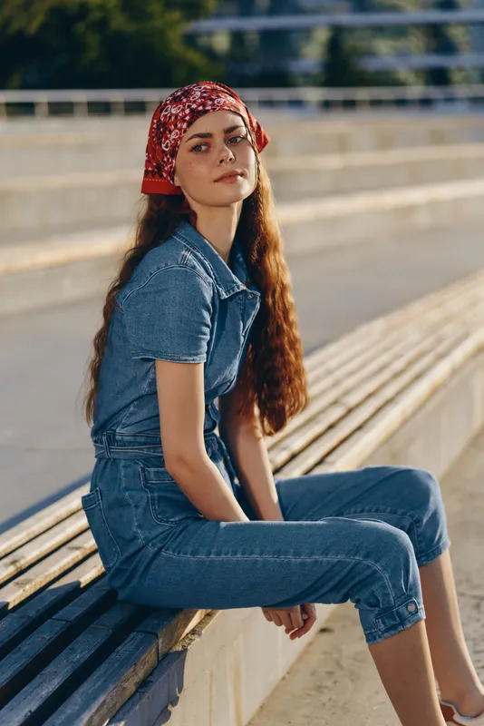 lifestyle woman in modern boho-western denim street style wearing a red bandana, sitting relaxed outdoors, film color tones enhancing natural light and mood