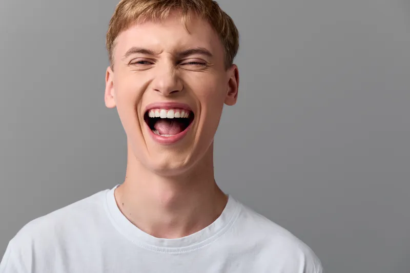 Laughter, open mouth smile, energetic young man wearing white tshirt in studio, conveying joy and excitement, upbeat mood, candid expression, vibrant happiness, dynamic pose, casual fashion