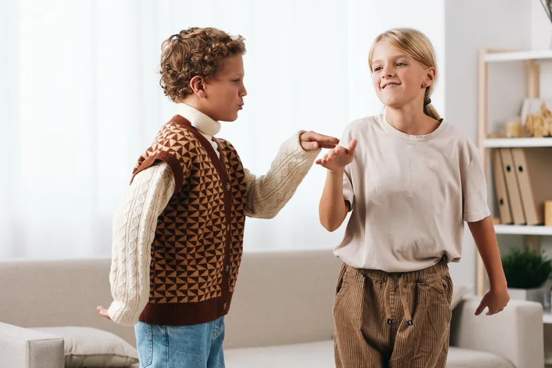 Two children share a joyful moment indoors, practicing a playful fist bump as they smile and move in a bright living space with soft light and cozy furniture.