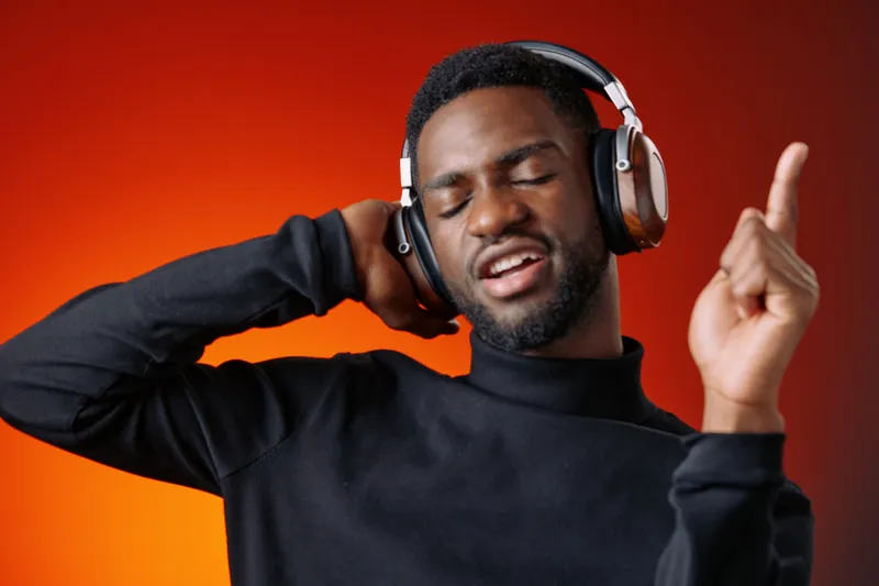 Joyful young man enjoying music with headphones, dancing to the beat against a vibrant orange background