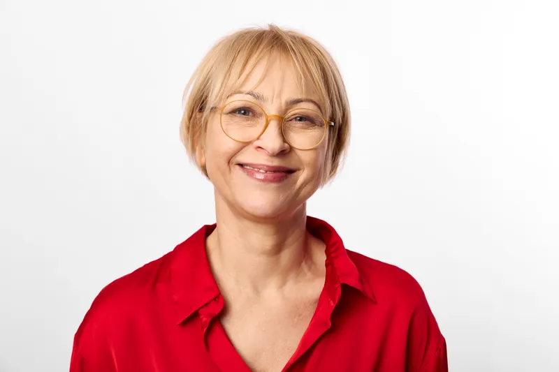 Elderly woman smiling portrait with glasses, red shirt, short blonde hair, studio headshot on white background, friendly calm mood, looking directly at camera