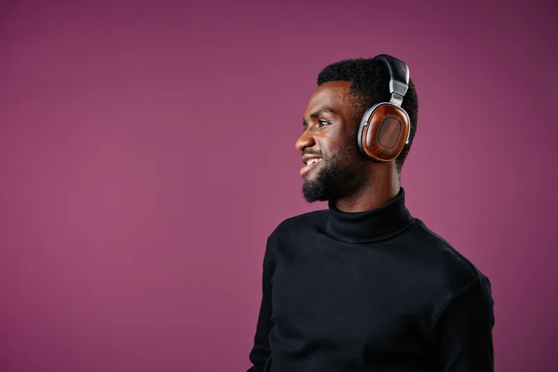 Young African man enjoying music with headphones against a purple background, smiling and showcasing a modern, stylish look