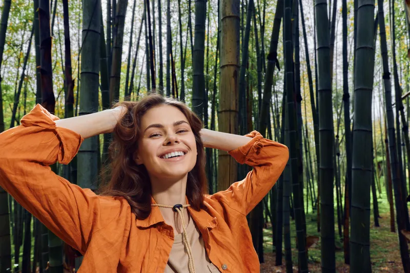 Smiling woman portrait in bamboo forest, nature outdoors scene showing happy relaxed female in casual orange jacket, enjoying peaceful green environment and natural lifestyle