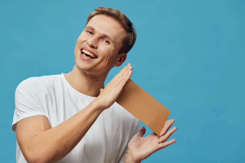 smiling man holding cardboard box isolated on blue background delivery parcel concept digital nomad happy courier casual white t-shirt