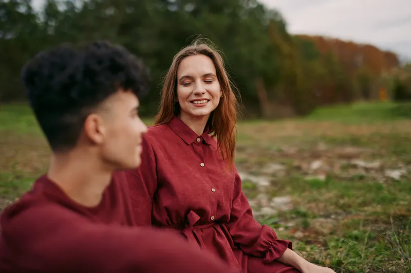 A candid outdoor portrait of two young people sharing a genuine moment on a grassy field, conveying authenticity and quiet connection through natural expressions, relaxed posture and soft autumn